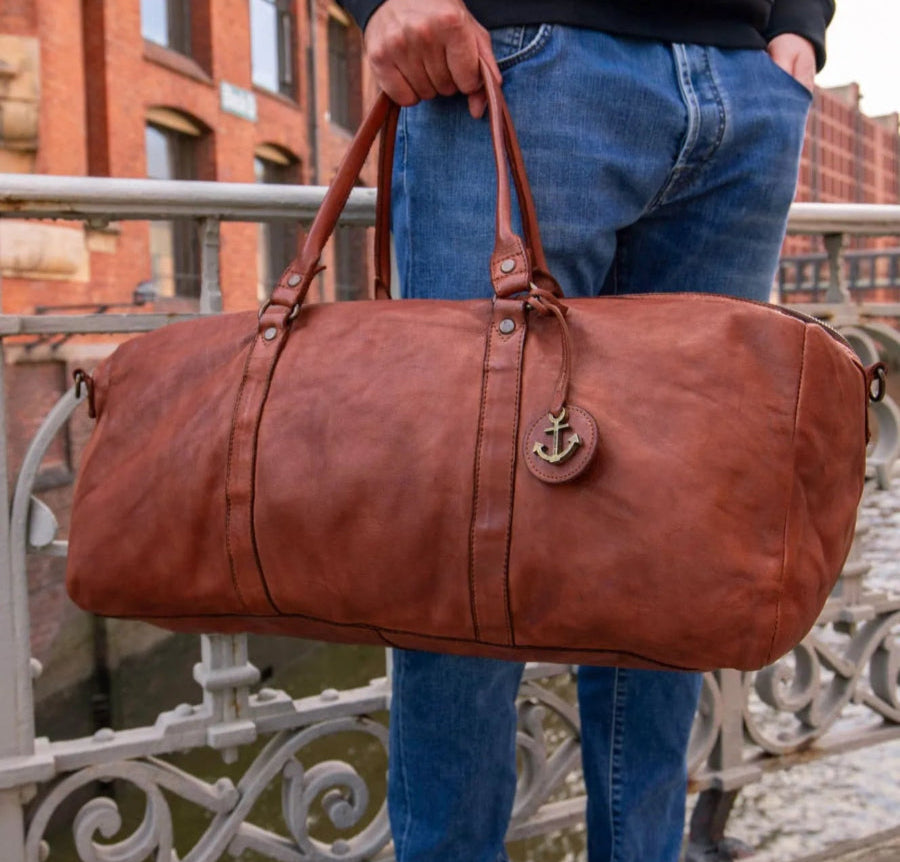 Mann am Wasser trägt Reisetasche aus Leder Modell Charming in Cognac